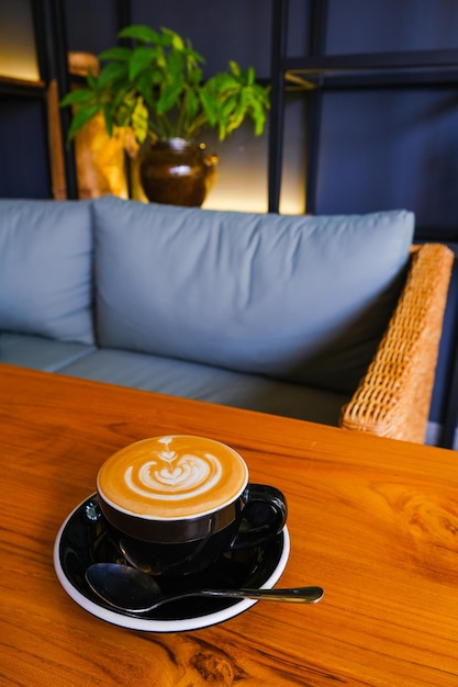 Black cup of cappuccino on wooden background with beautiful latte art