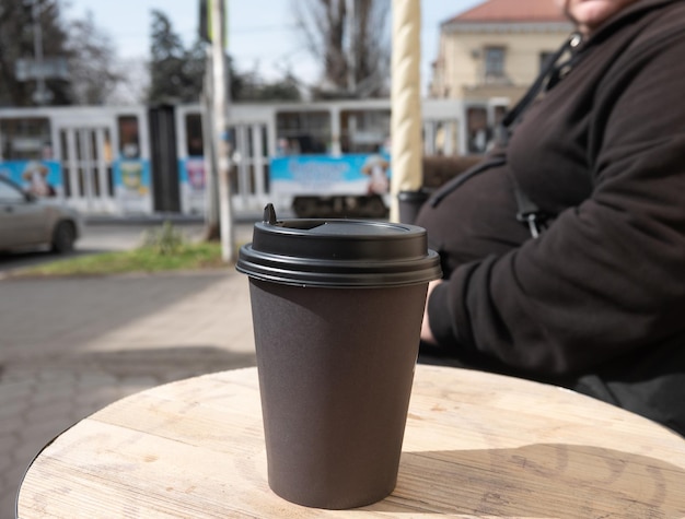 A black cup of coffee sits on a round table in front of a woman.