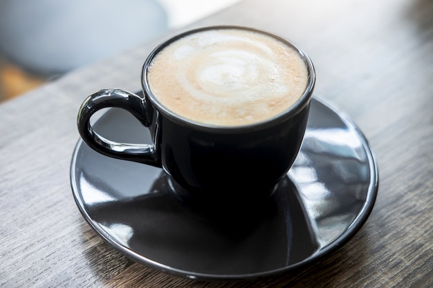 Black Cup of coffee with milk foam so delicious on old wooden table