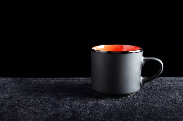 Black cup colored orange inside on dark surface and black background