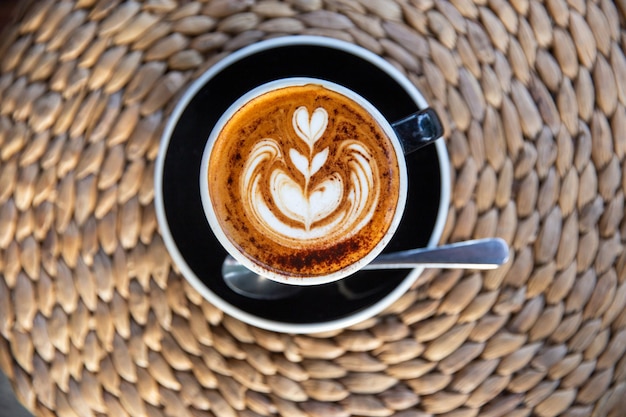 Black cup of tasty cappuccino with latte art on bamboo background in cafe