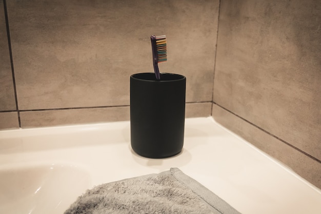 Black cup for a toothbrush on the background of a gray bathroom