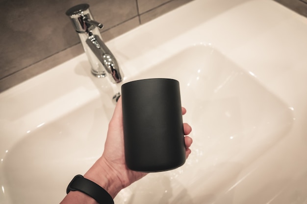 Black cup for a toothbrush on the background of a gray bathroom