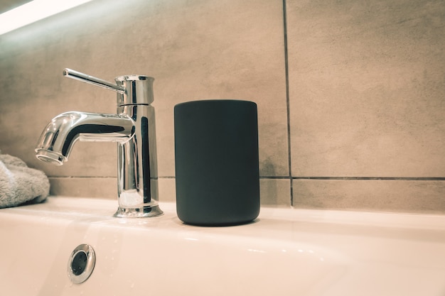 Black cup for a toothbrush on the background of a gray bathroom