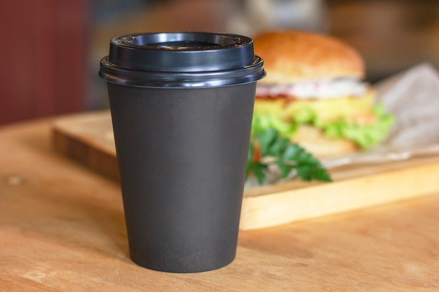 Photo black cup with coffee to go on background with burger, mock up