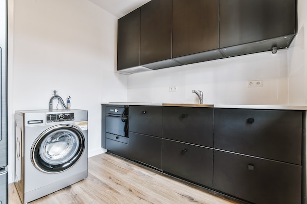 Black cupboards with stove and sink located near contemporary washing machine in kitchen of apartment