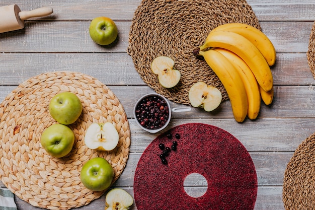 Black currant fruit leather with fresh fruits on the wooden table. Round red fruit leather with black currant. Healthy food. Apples, bananas top view.