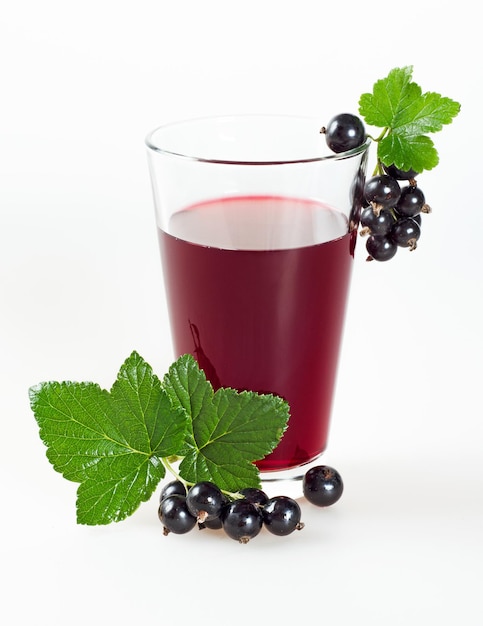 Black currant juice in a glass and ripe berries with green leaves on a white background.