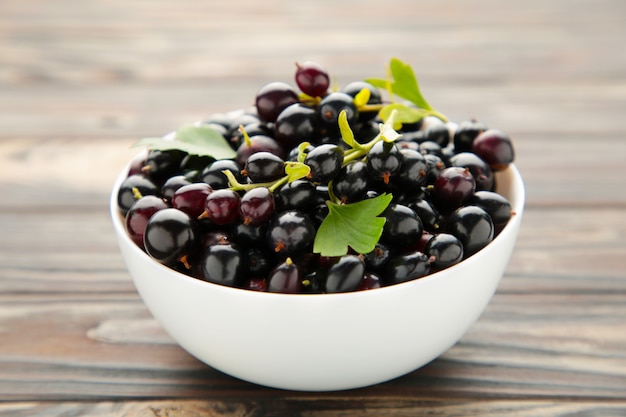 Black currant in a white bowl on brown wooden background