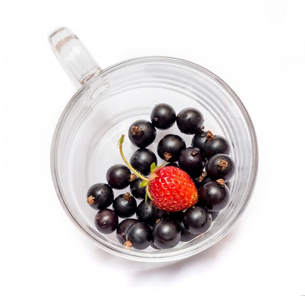 Black currant with strawberry in a transparent glass cup isolated