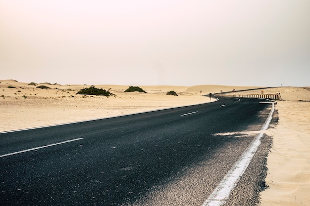 black dark asphalt road in the middle of the desert and sandy dunes