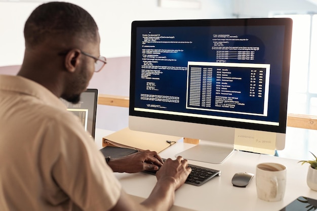 オフィスでコンピューターで作業するときにソフトウェアをデバッグする眼鏡をかけた黒人の開発者