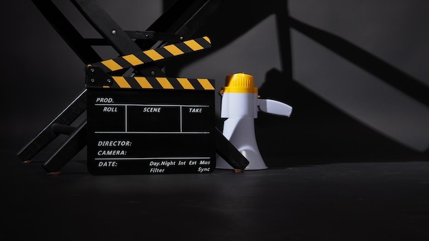 Черный режиссерский стул и доска с хлопушкой или кинохлопушка с мегафоном на черном фоне используется в видеопроизводстве или киноиндустрии