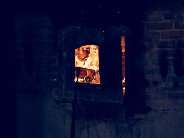 어두운 유리 공장에서 그을음으로 덮인 벽돌 벽에 밝은 타는 불꽃이 있는 검은 더러운 용광로