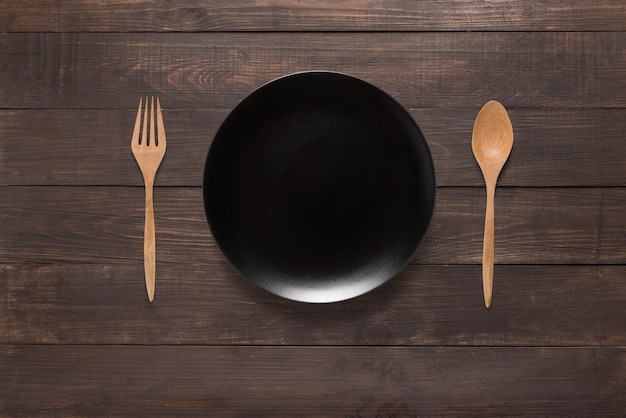 Black dish, fork and spoon on the wooden background. Top view