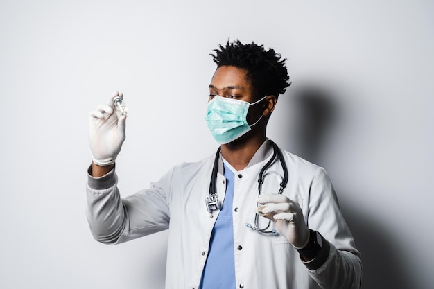 Black doctor in medical mask is holding vaccine on white background Handsome African doctor with coronavirus covid19 vaccine