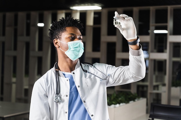 Black doctor with 2 doses of vaccine Booster vaccination African doctor in medical mask is holding vaccines in hand