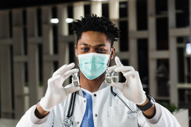 Black doctor with 3 doses of vaccine Booster vaccination African doctor in medical mask is holding vaccines in hand