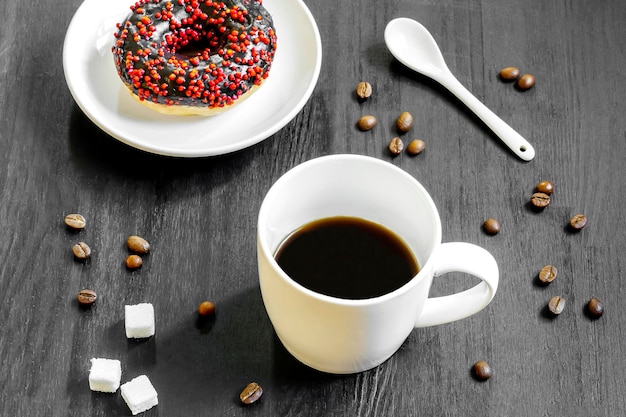 초콜릿 글레이즈로 덮인 블랙 도넛은 식탁에 커피 콩을 곁들인 접시에 에스프레소 커피 음료 맛있는 달콤한 설탕 크림 또는 아이싱 도넛 디저트 음식을 제공합니다.