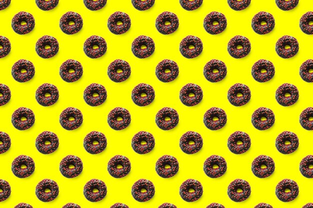 Black donuts with red glaze on yellow background seamless pattern top view. Food dessert flatly flat lay of delicious sweet nibbles chocolate donuts.