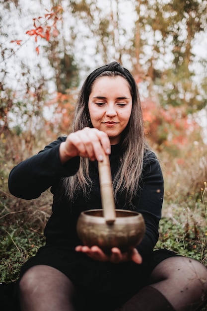 Donna buddista vestita di nero che tiene e suona una campana tibetana con un bastone di legno.