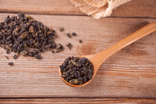 Photo black dry tea leaves with wooden spoon on the wooden table