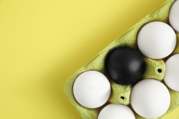 Black egg among others in box on yellow background top view Space for text