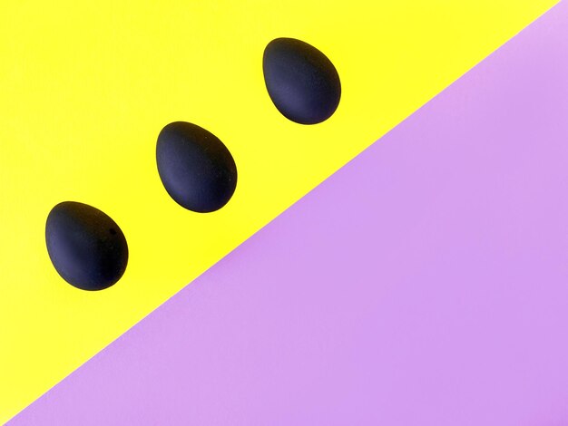 黄色と紫の背景に黒い卵イースター多様性幾何学模様食品コンセプト