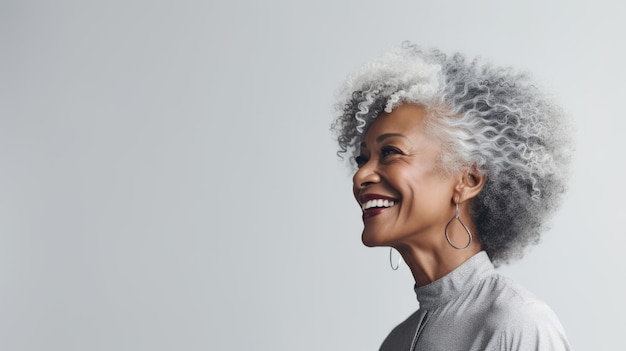 灰色のアフロヘアの黒人高齢女性が笑顔を浮かべ浅い灰色のスタジオの背景にポーズをとって5060年間肌のケアをしています