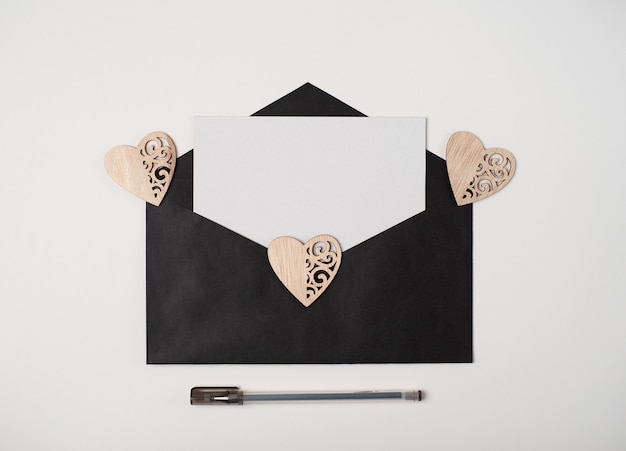 Black envelope with a blank sheet inside and wooden hearts on white. Love letter for Valentine's day concept.