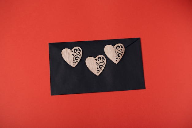 Black envelope with three wooden hearts on the red background. Valentine's Day concept.