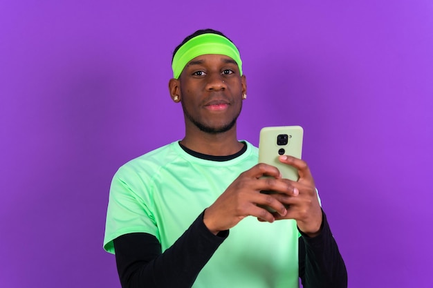 Black ethnic man holding a phone in green sportswear isolated on purple colored background