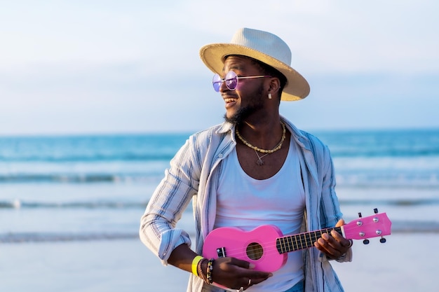 Black ethnic man playing ukulele by the sea enjoying summer vacation on the beach