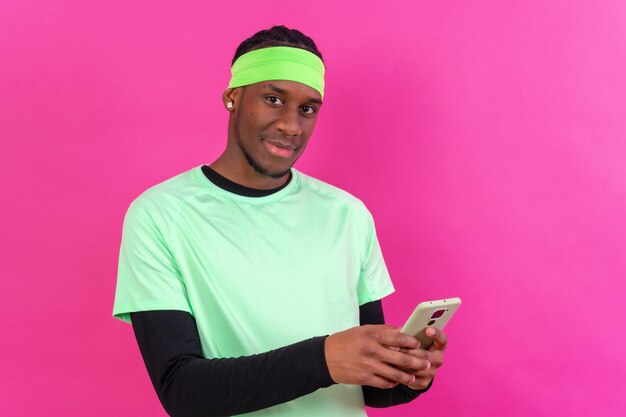 Black ethnic man with a phone in green clothes on a pink background smiling