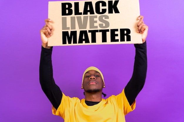 Uomo etnico nero in abiti gialli su sfondo viola che punta tenendo un cartello che le vite nere contano