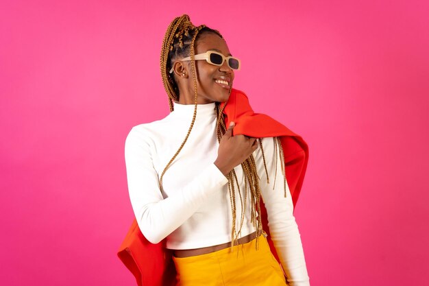 Black ethnic woman with braids on a pink background wearing a red suit and white tshirt smiling