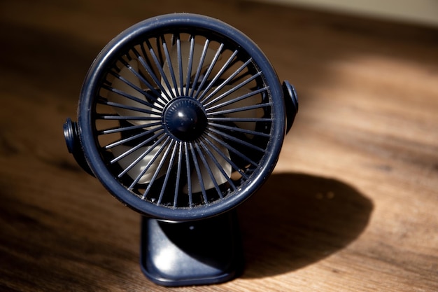A black fan sits on a table with a shadow on the table.
