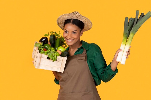 Black farmer lady holding box with fresh harvest yellow background