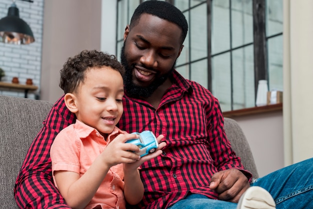 Photo black father and son playing with blue toy car