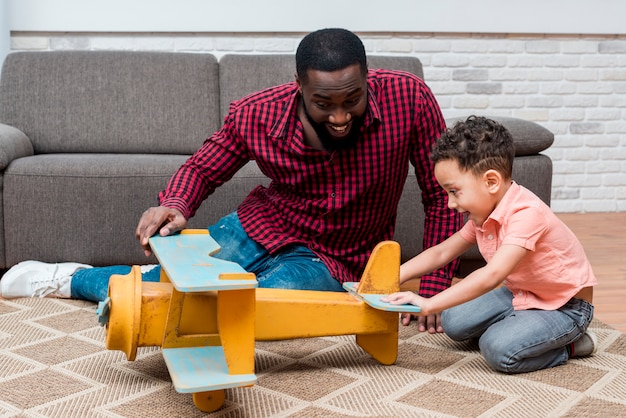 Photo black father and son playing with toy plane