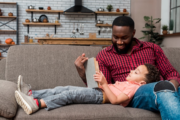 Black father and son reading book on couch