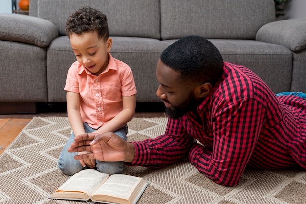 Black father and son reading book on floor