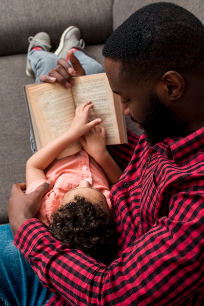 Black father and son reading book on sofa