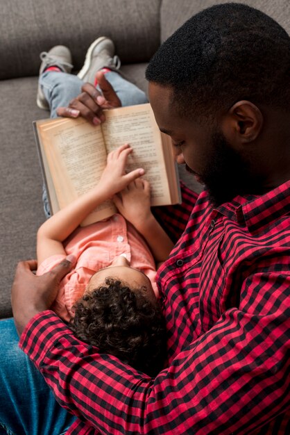 Black father and son reading book on sofa