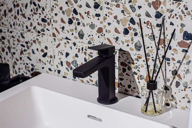 Черный смеситель на умывальнике в ванной, стена украшена плиткой в стиле терраццо