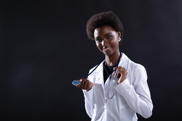 Black female doctor smiling at black background African american woman in medical gown with stethoscope standing and smiling