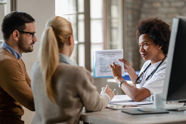 Black female doctor talking to a couple while showing them test results in their medical report