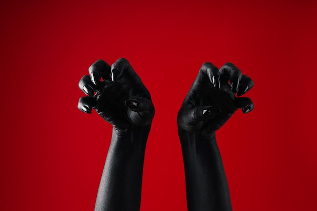 Black female hands with black manicure on red background