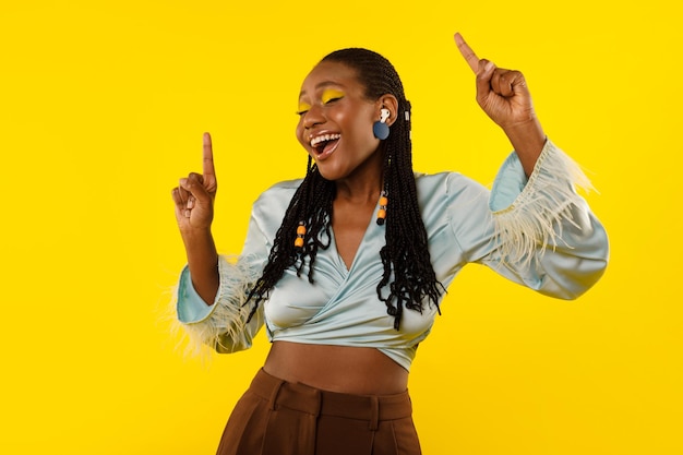 Black female listening to music via earbuds over yellow background