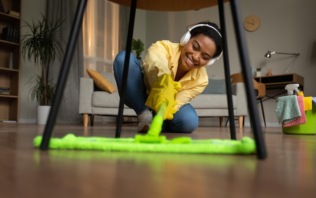 Black female mopping floor listening music wearing earphones at home